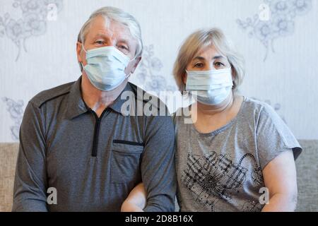 Les masques protecteurs sont des visages de personnes âgées, couple senior assis sur un canapé à la maison Banque D'Images