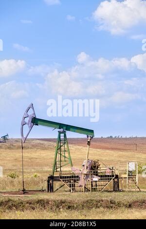 Vérin de pompe à huile en fonctionnement sur terrain agricole, ciel bleu, image verticale Banque D'Images