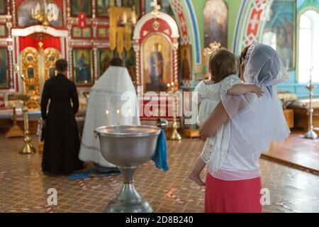 Marraine avec sa fille sur les bras se tenant près du baptistère Au cours de la cérémonie de baptême dans l'église russe Banque D'Images