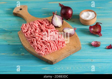 La viande hachée et les oignons rouges sont sur une planche à découper en bois. Salière sur une table en bois bleu Banque D'Images