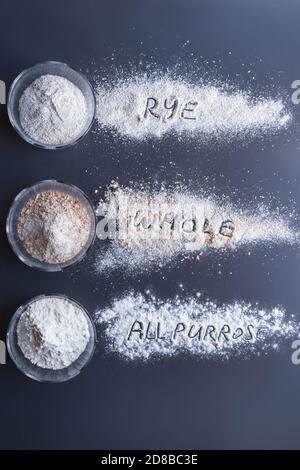 farines pour faire du pain dans des tasses en verre: seigle, blé complet, farine ordinaire ou polyvalente ou forte disposée sur fond gris Banque D'Images