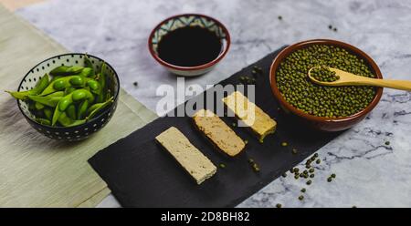 Différents produits dérivés du soja. Haricots édamames, sauce soja, tofu, tempeh et soja. Repas sur une nappe sur un comptoir en marbre. Banque D'Images
