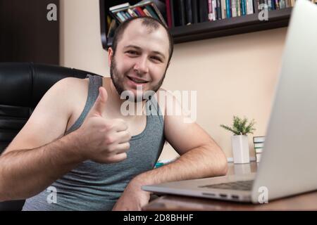Loisirs avec un ordinateur portable. Un jeune homme barbu dans des vêtements maison T-shirt gris, utilise un ordinateur portable pour regarder des vidéos, jouer à des jeux, communiquer, trolling Internet, Banque D'Images