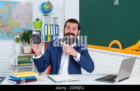 homme heureux avec la barbe calculant sur la calculatrice dans la leçon de mathématiques à l'école, les mathématiques. Banque D'Images