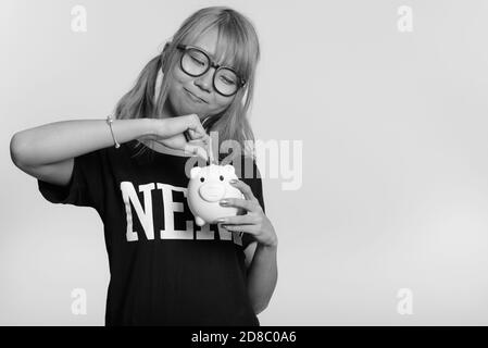 Young cute Asian nerd woman putting coins in piggy bank Banque D'Images
