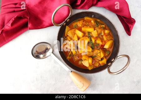 Pommes de terre indiennes épicées maison et curry de tomates également connu sous le nom d'aloo tamatar ki sabji en hindi, servi dans un kadai de fer avec des spatules souriantes. Copier l'espace. Banque D'Images