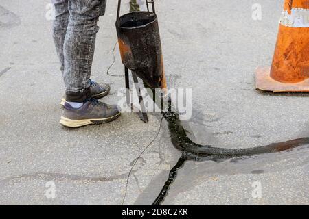 Homme scellant l'allée de l'asphalte avec des fissures remplies scellant accent sélectif Banque D'Images