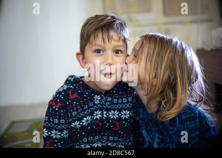 Deux frères et sœurs en pyjama avec livre, soeur baiser frère, drôle émotions énorme maison Banque D'Images