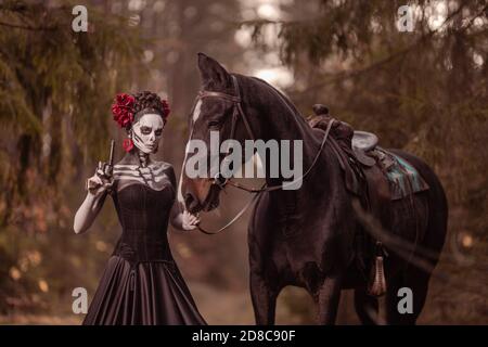 Jeune femme habillée comme le symbole mexicain de l'époque de la calavera morte dans une robe noire posant dans la forêt avec un cheval Banque D'Images