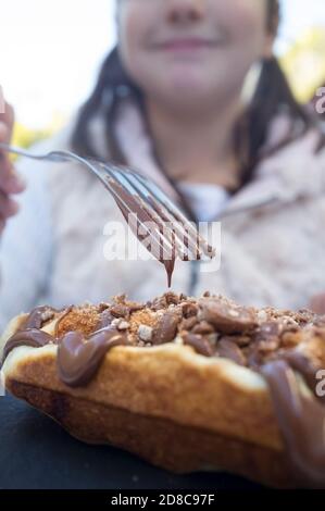 Petite fille mangeant des gaufres couvertes de garniture au chocolat noir et de céréales en poudre. Gros plan de la fourche goutte à goutte Banque D'Images