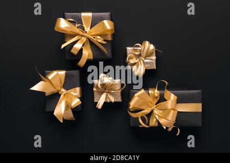 Boîtes-cadeaux dorées emballées de façon festive sur fond noir. Style de pose à plat. Concept des fêtes et du Vendredi fou Banque D'Images