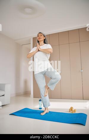 Femme attentionnée dans un vêtement de sport debout sur un tapis de yoga dans la chambre intérieur Banque D'Images