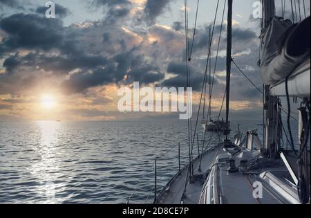 Fragment de luxueux yacht riche dans la mer Méditerranée pendant un coucher de soleil pittoresque et lumineux, soleil nuageux ciel et horizon sur l'eau bleue calme. C Banque D'Images