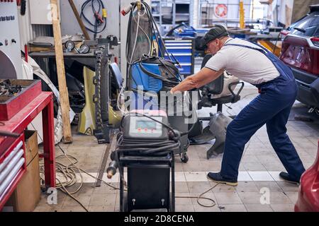 Mécanicien automobile utilisant le chargeur de batterie à l'atelier de réparation automobile Banque D'Images