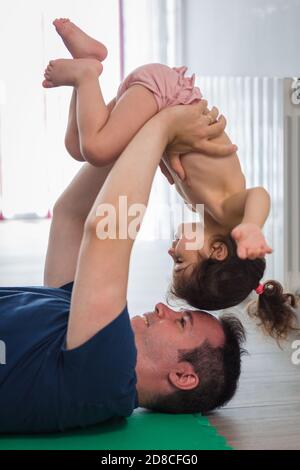 Le père caucasien fait du sport, de la forme physique et du yoga avec sa petite fille de mère latine dans la salle à manger de la maison, ils ont du plaisir pendant qu'ils font l'exe Banque D'Images