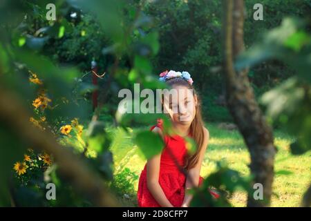 Beauté romantique fille plein air. Belle adolescente modèle en robe rouge est assis sur le jardin dans la lumière du soleil. Cheveux longs soufflants Banque D'Images