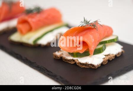 Canapés au poisson rouge, concombres et fromage doux sur une assiette d'ardoise Banque D'Images