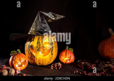 Citrouilles sculptées pour Halloween, la tête de Jack est sur la table. Citrouille dans un chapeau de sorcière. Arrière-plan sombre. Banque D'Images