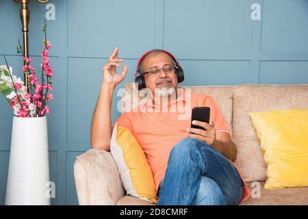 Vieil homme asiatique indien utilisant un casque tout en écoutant de la musique ou regarder des films sur une tablette ou un smartphone Banque D'Images