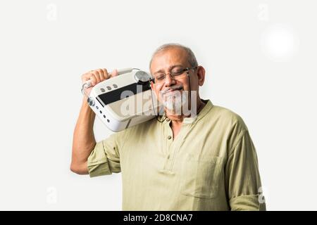 Un vieil homme asiatique indien ou un homme adulte de premier plan écoutant de la musique sur une radio d'époque en utilisant des écouteurs et en dansant, isolé sur fond blanc Banque D'Images