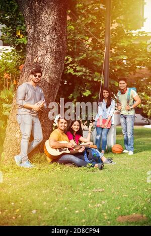 Des étudiants indiens asiatiques jouant de la musique avec de la guitare tout en étant assis dans le campus sur les escaliers ou sur la pelouse Banque D'Images