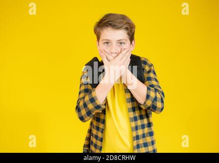 Mignon petit garçon couvre sa bouche et regarde la caméra, sur fond jaune Banque D'Images