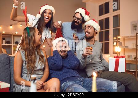 Groupe de jeunes amis qui boivent du champagne, qui s'amusent et jouent à des jeux amusants lors d'une fête à la maison. Banque D'Images