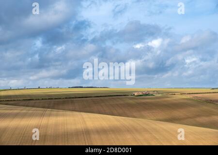 Vue sur une ferme abandonnée sur des champs à rayures labourés par une journée ensoleillée avec un ciel nuageux. Banque D'Images