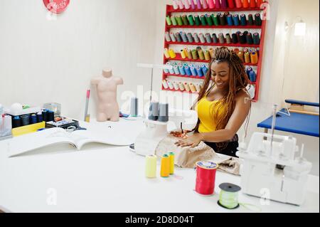 Une jeune couturière africaine cousue des vêtements sur une machine à coudre au bureau sur mesure. Femmes de couturière noires. Banque D'Images