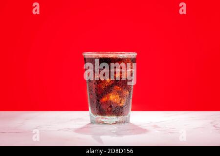 Verre froid glacé de soda, boisson gazeuse, cola, pop avec glaçons et condensation sur un fond rouge avec espace de copie et espace pour le texte. Banque D'Images