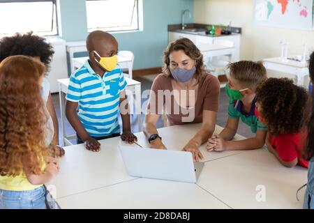 Une enseignante portant un masque facial utilisant un ordinateur portable pour enseigner aux élèves en classe Banque D'Images