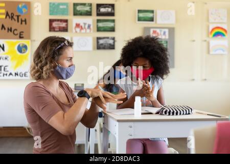 Une enseignante portant un masque facial aidant une fille à se désinfecter ses mains en classe Banque D'Images