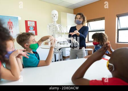 Enseignante portant un masque facial utilisant un modèle de squelette humain à enseigner aux élèves en classe Banque D'Images