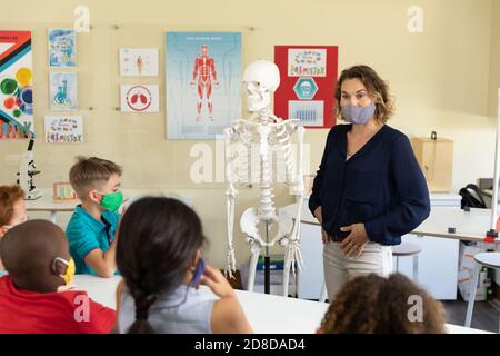 Enseignante portant un masque facial utilisant un modèle de squelette humain à enseigner aux élèves en classe Banque D'Images