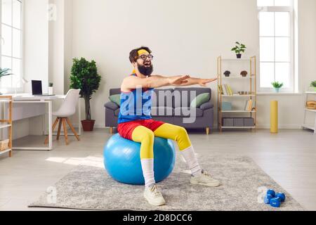 Riant drôle barbu homme dans des vêtements de sport brillant faisant warkout sur ballon de fitness à la maison Banque D'Images