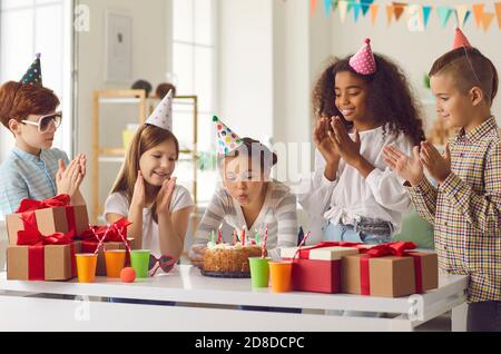 Une petite fille d'anniversaire souffle des bougies sur un gâteau aux applaudissements de ses amis internationaux. Banque D'Images