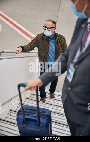 Homme d'affaires en lunettes montant les marches de l'avion Banque D'Images