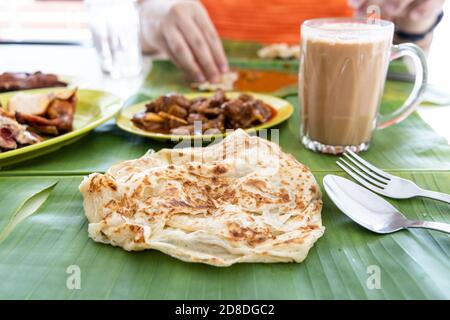 Roti canai ou paratha servi sur une feuille de banane, avec du curry de mouton et du poulet frit, et du thé populaire tarik Banque D'Images