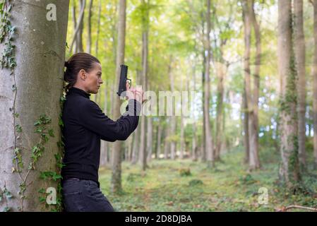 Femme tenant un pistolet, avec son dos contre un arbre. Banque D'Images