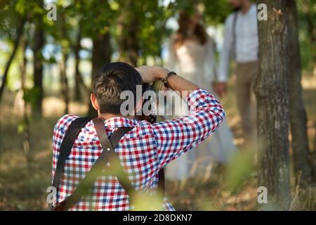 photographe professionnel de mariage prend des photos de la mariée et marié dans le parc en journée ensoleillée, homme photographe en action Banque D'Images