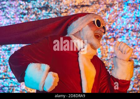 Homme barbu en lunettes de soleil et en costume de Père Noël courant à la fête Banque D'Images