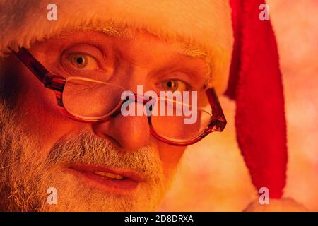 Gros plan d'un homme barbu senior dans un chapeau de père Noël et dans lunettes regardant l'appareil photo Banque D'Images