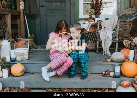 enfants un garçon et une fille en pyjama et de protection masque facial avec un panier de bonbons sur le porche de l'arrière-cour décoré avec des citrouilles en automne Banque D'Images