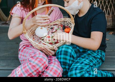 enfants un garçon et une fille en pyjama et de protection masque facial avec un panier de bonbons sur le porche de l'arrière-cour décoré avec des citrouilles en automne Banque D'Images