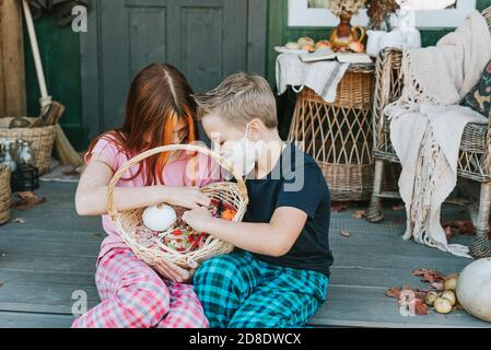 enfants un garçon et une fille en pyjama et de protection masque facial avec un panier de bonbons sur le porche de l'arrière-cour décoré avec des citrouilles en automne Banque D'Images