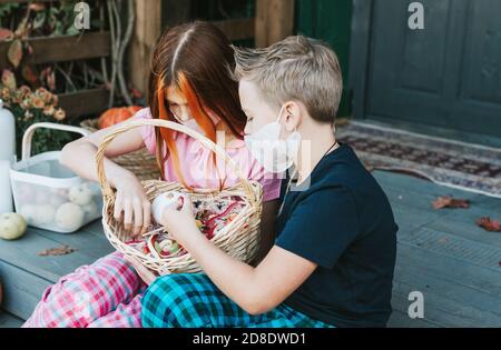 enfants un garçon et une fille en pyjama et de protection masque facial avec un panier de bonbons sur le porche de l'arrière-cour décoré avec des citrouilles en automne Banque D'Images