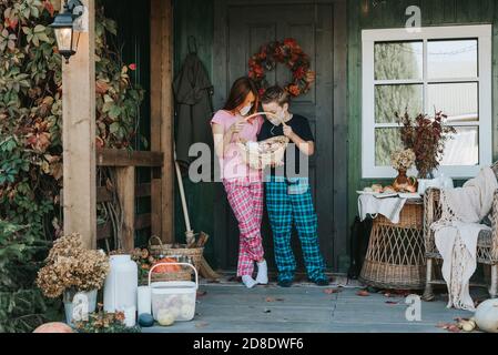 enfants un garçon et une fille en pyjama et de protection masque facial avec un panier de bonbons sur le porche de l'arrière-cour décoré avec des citrouilles en automne Banque D'Images