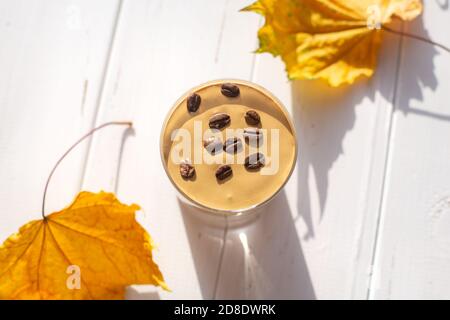 Boisson traditionnelle au lait caféiné coréen, café Dalgona dans un verre avec grains de café sur fond de tableau blanc. Feuilles d'érable sèches. Petit déjeuner d'automne Banque D'Images