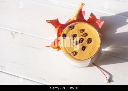 Boisson traditionnelle au lait caféiné coréen, café Dalgona dans un verre avec grains de café sur fond de tableau blanc. Rouge érable sec eav. Breakfas d'automne Banque D'Images