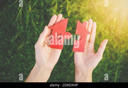 Maison rouge avec une forme de deux parties de puzzle dans les mains humaines. Banque D'Images